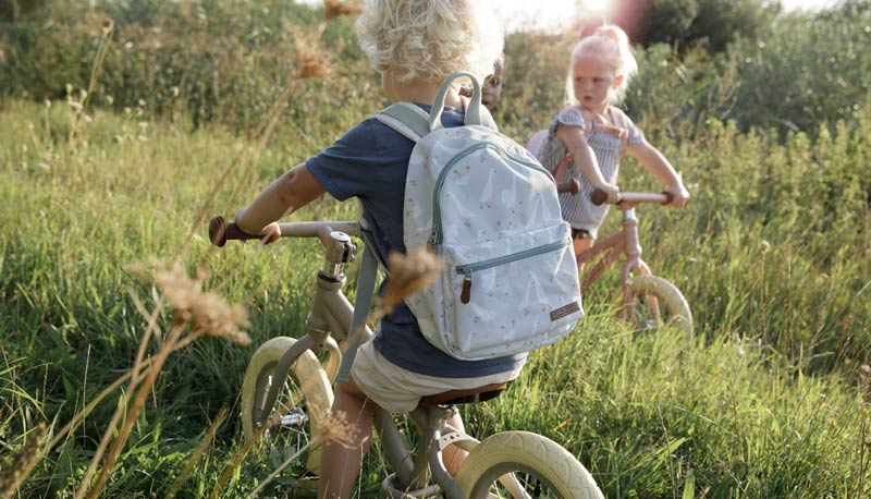Two kids riding bikes outdoors with little backpacks