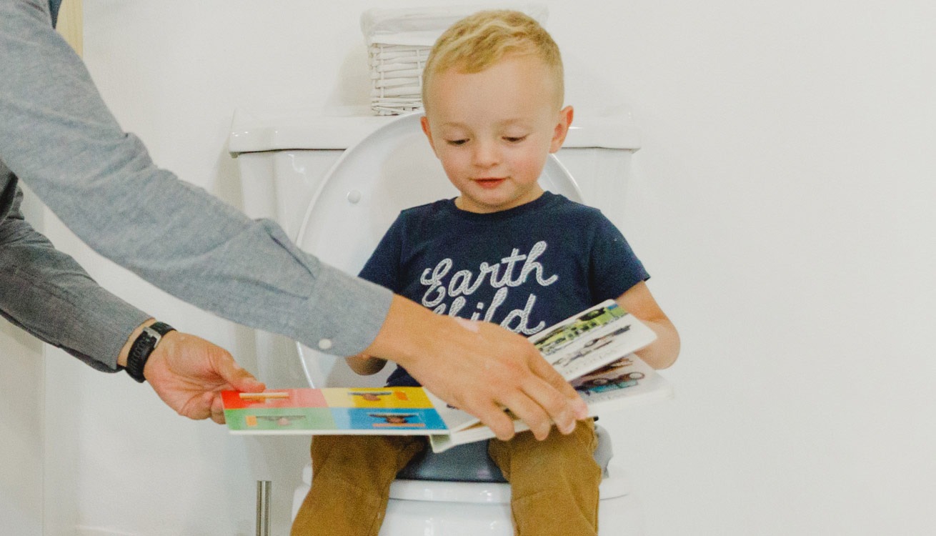 A boy reading while using the Bumbo Toilet Trainer